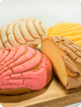 Four colorful Mexican sweet breads, known as Conchas, on a wooden board.