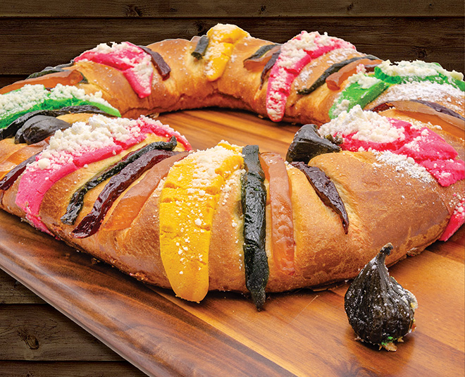A colorful Rosca de Reyes bread with multicolored toppings on a wooden board.