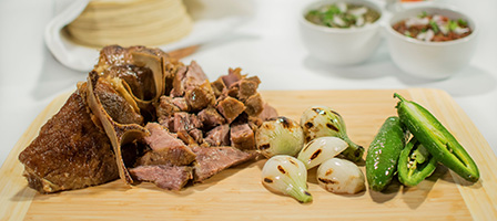 Chopped meat with grilled onions and green peppers on a wooden board.