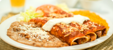 A plate of enchiladas with refried beans, rice, and salad garnish.