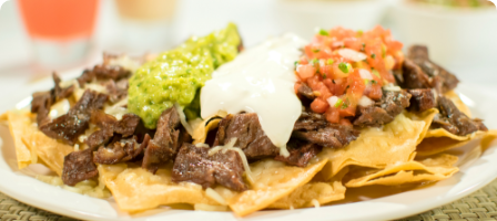 Plate of nachos topped with grilled beef, guacamole, sour cream, and salsa.