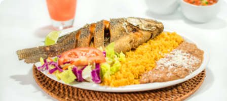 A plate with cooked fish, yellow rice, and refried beans, garnished with lettuce and cabbage