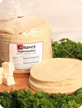 Package of Chavez corn tortillas with loose tortillas and cheese cubes on a wooden surface.